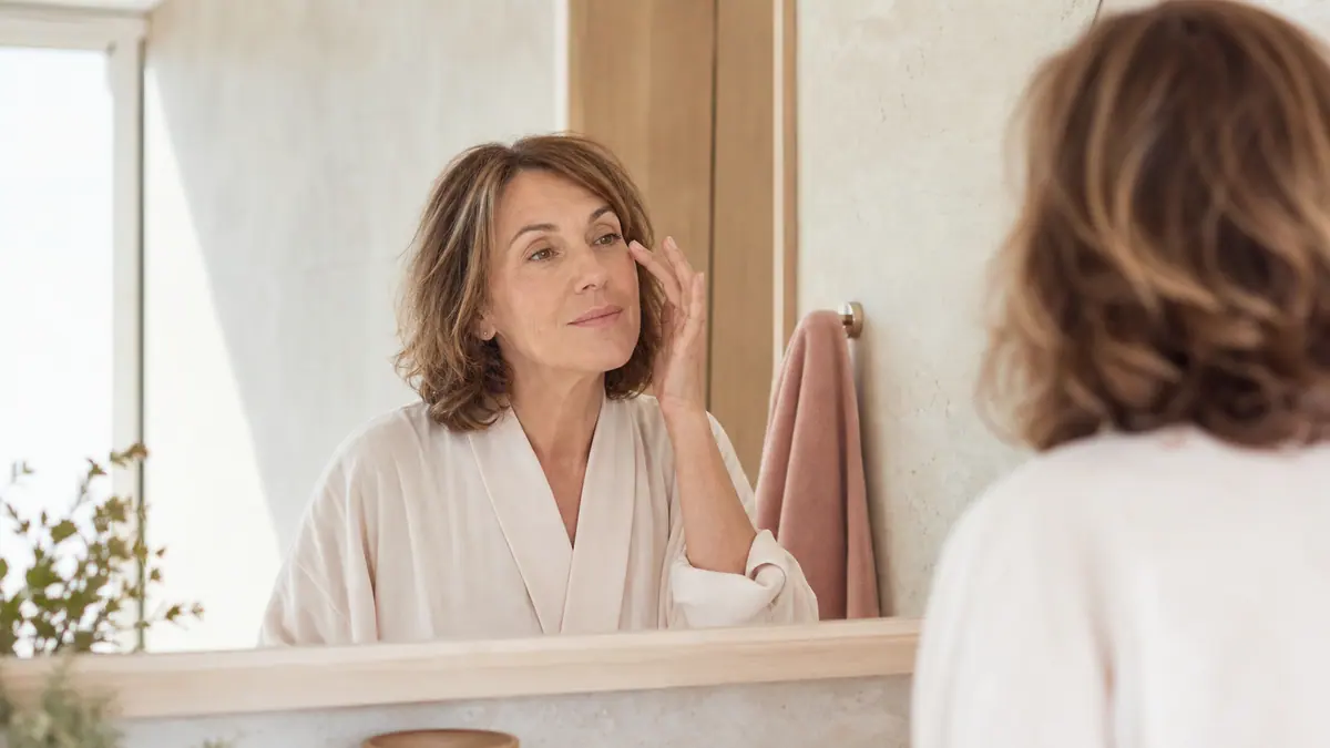 Mulher madura observando suavemente a região dos olhos no espelho pela manhã